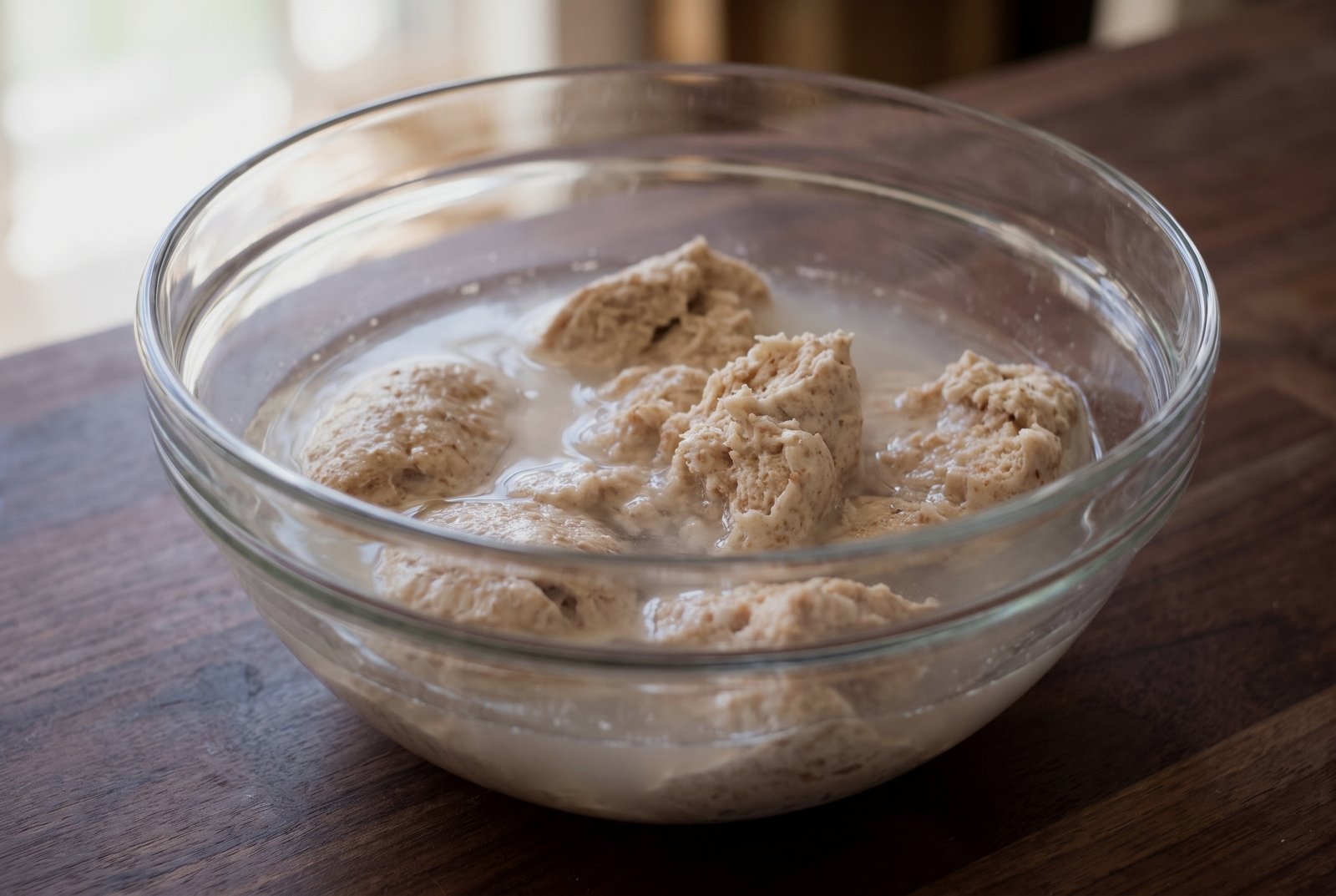 Stiff starter pieces dissolving in recipe water in a mixing bowl before flour is added