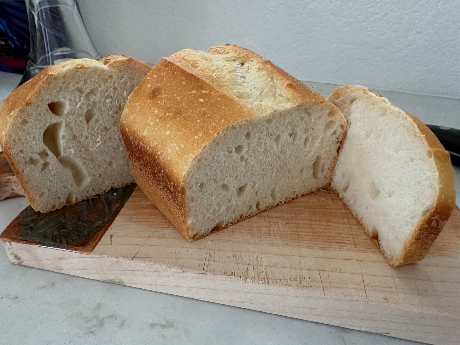 Sliced sandwich loaf with golden crust and open crumb on a wooden cutting board