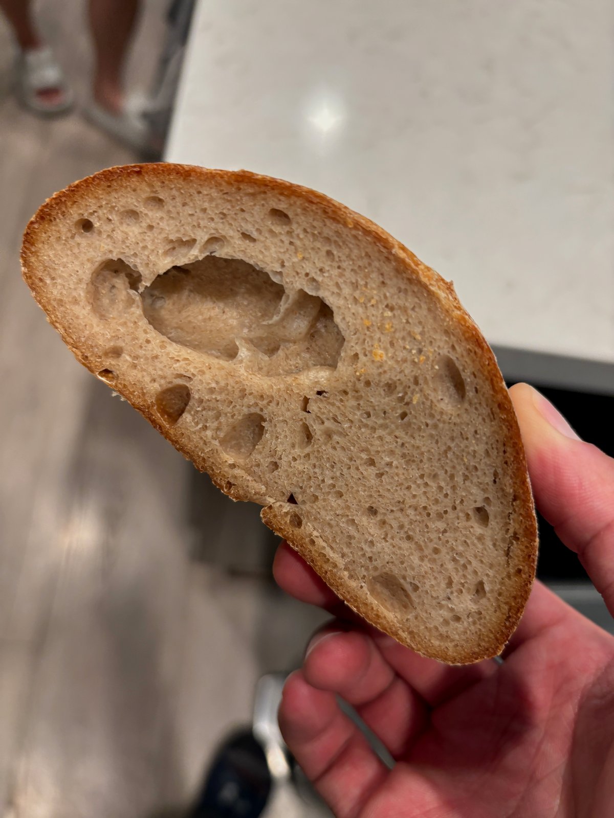 Under-fermented artisan crumb with a large tunnel void in a dense, tight matrix