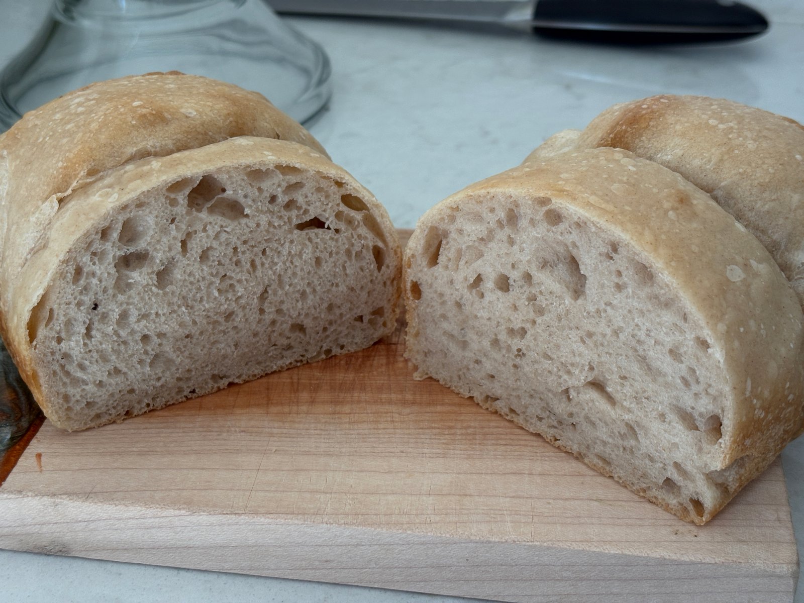 Sliced whole wheat sandwich loaf with golden crust and open custardy crumb on a wooden cutting board